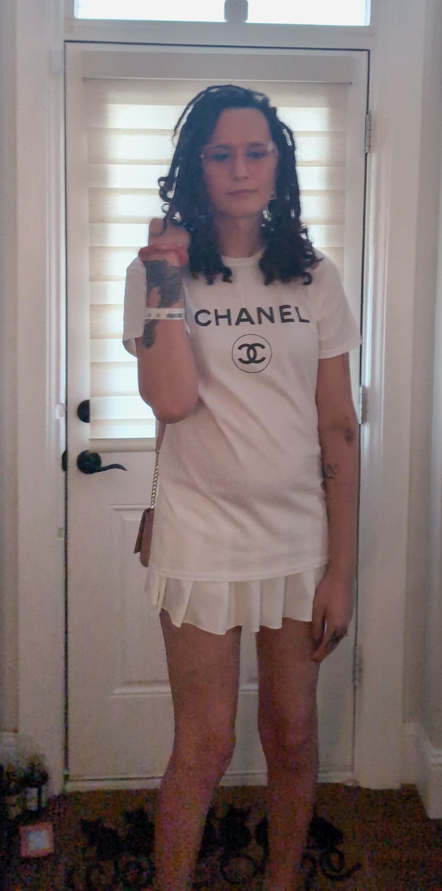 Picture of me standing in front of a door wearing a Chanel T shirt and a mini skirt and I'm holding my purse behind my shoulder with my right hand.